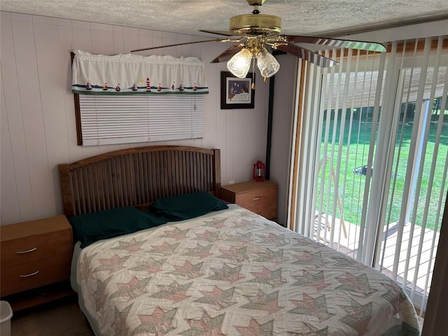 bedroom featuring access to outside, ceiling fan, wooden walls, and a textured ceiling