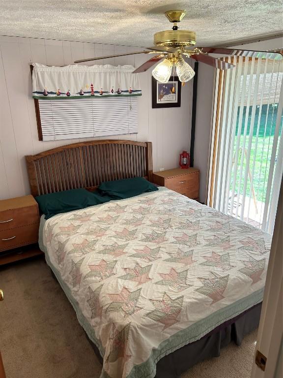 bedroom with carpet flooring, ceiling fan, wood walls, and a textured ceiling