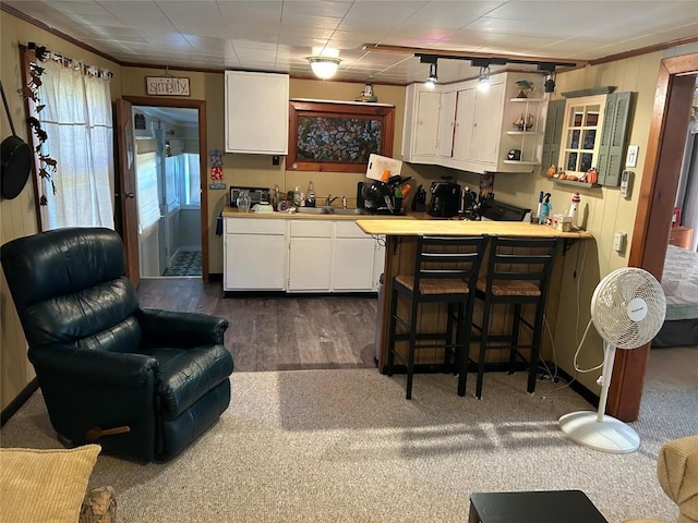 kitchen featuring dark carpet, crown molding, sink, white cabinetry, and a breakfast bar area