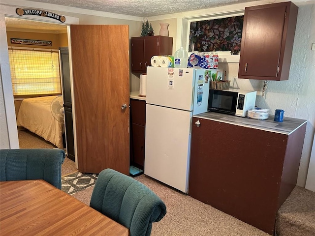 kitchen featuring dark brown cabinets, white appliances, a textured ceiling, and light carpet