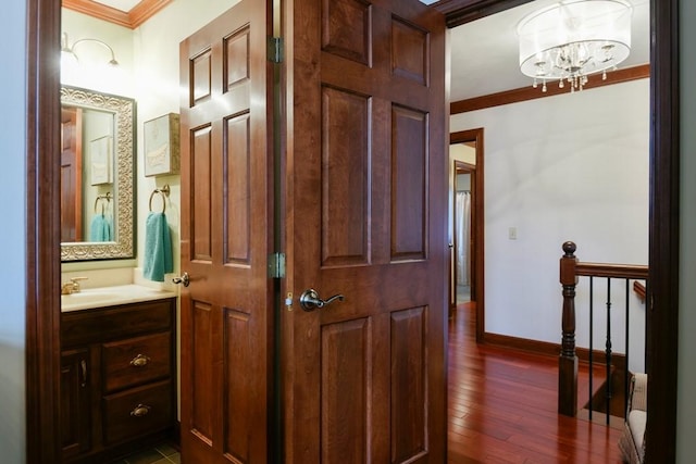 corridor with an inviting chandelier, ornamental molding, dark hardwood / wood-style flooring, and sink