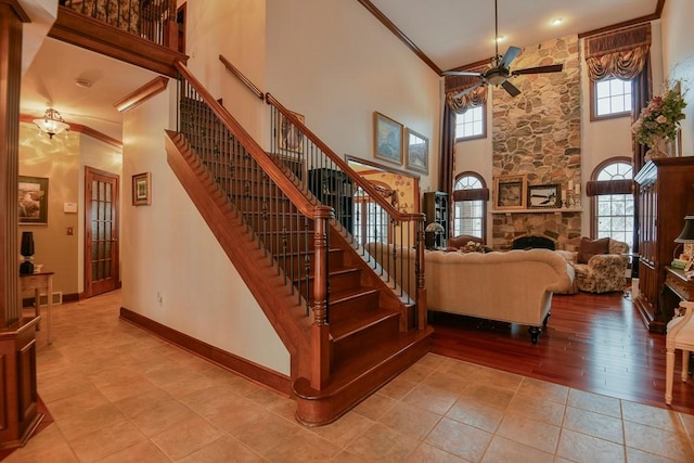 stairway with tile patterned flooring, a stone fireplace, crown molding, ceiling fan, and a high ceiling