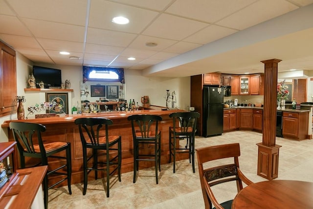 bar featuring a paneled ceiling, black refrigerator, and decorative columns