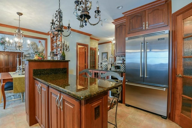 kitchen featuring a center island, built in refrigerator, dark stone countertops, hanging light fixtures, and crown molding