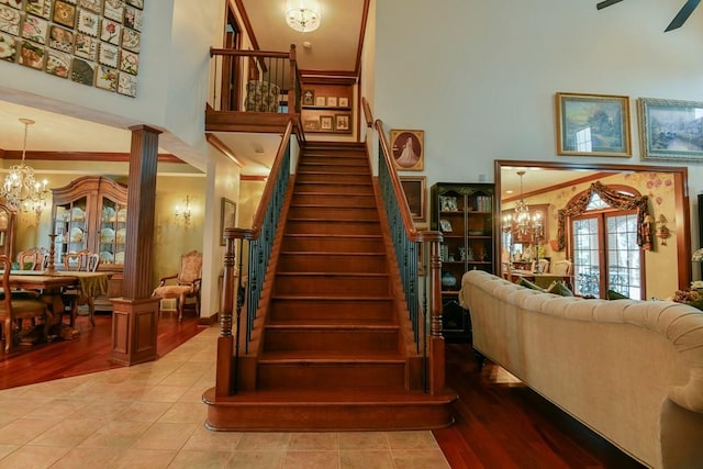 staircase with hardwood / wood-style floors, crown molding, ceiling fan with notable chandelier, and decorative columns