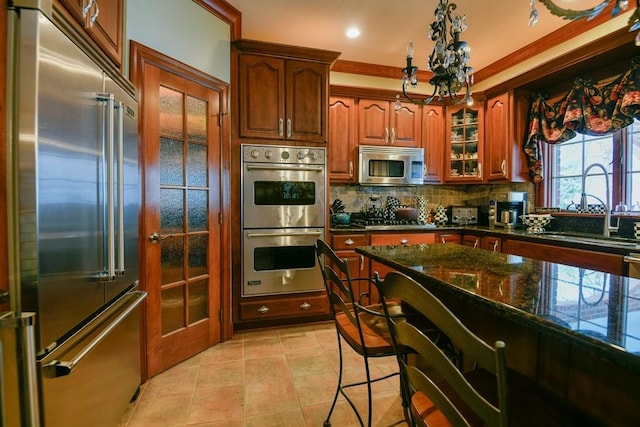 kitchen with dark stone countertops, appliances with stainless steel finishes, a breakfast bar, sink, and tasteful backsplash