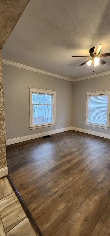 empty room with ceiling fan, dark wood-type flooring, and ornamental molding