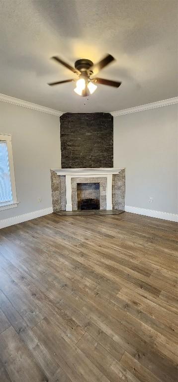 unfurnished living room with ceiling fan, a large fireplace, wood-type flooring, and ornamental molding