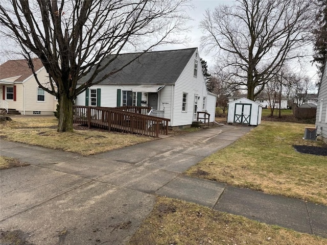 view of front of property featuring a shingled roof, an outbuilding, a front lawn, and a shed