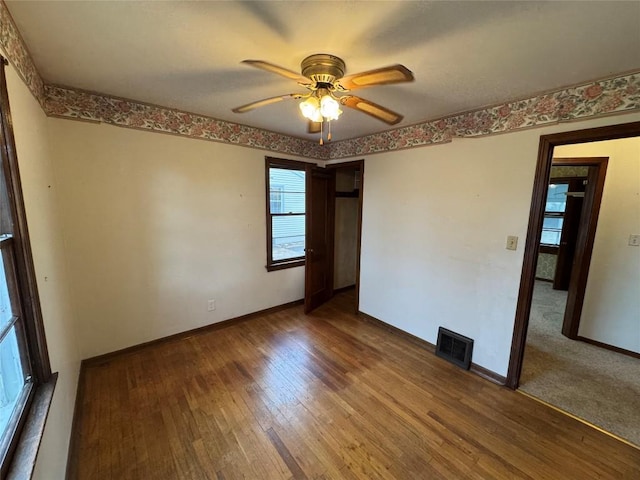 empty room featuring ceiling fan, wood finished floors, visible vents, and baseboards