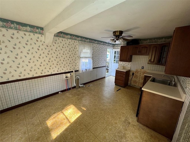 kitchen with a wainscoted wall, light countertops, ceiling fan, a sink, and wallpapered walls