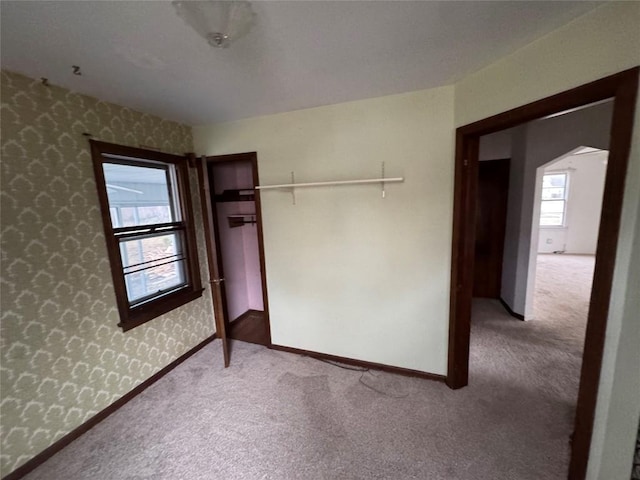 unfurnished bedroom featuring baseboards, arched walkways, carpet flooring, and wallpapered walls