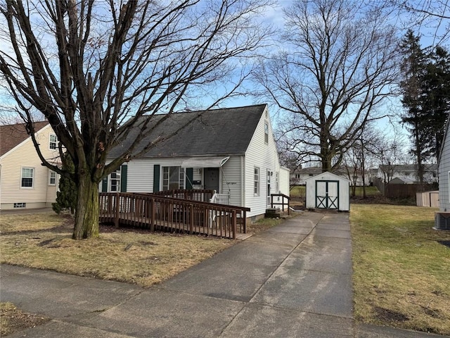 view of front of home with an outdoor structure, roof with shingles, a storage unit, a wooden deck, and a front lawn