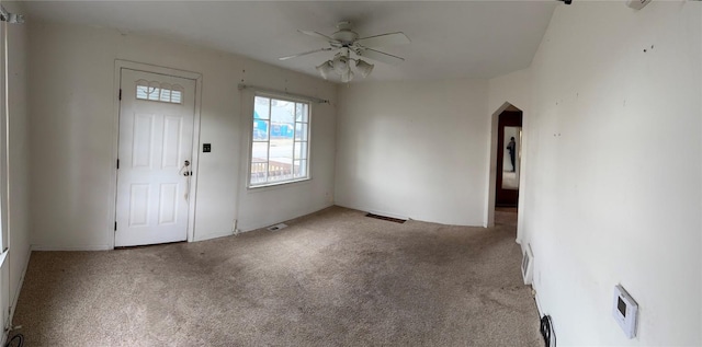 carpeted foyer with a ceiling fan, arched walkways, and visible vents