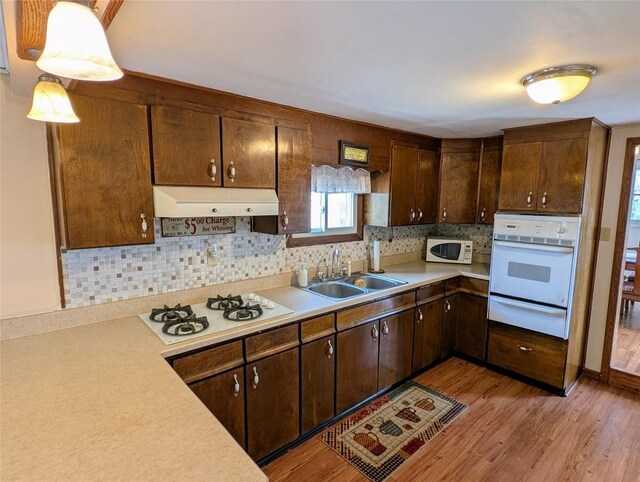 kitchen featuring white appliances, light countertops, a warming drawer, light wood-style floors, and a sink