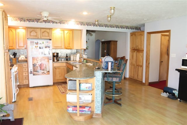 kitchen with light brown cabinets, tasteful backsplash, kitchen peninsula, white appliances, and a breakfast bar