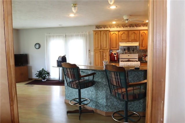 kitchen featuring gas range gas stove, ceiling fan, a kitchen breakfast bar, backsplash, and light hardwood / wood-style floors