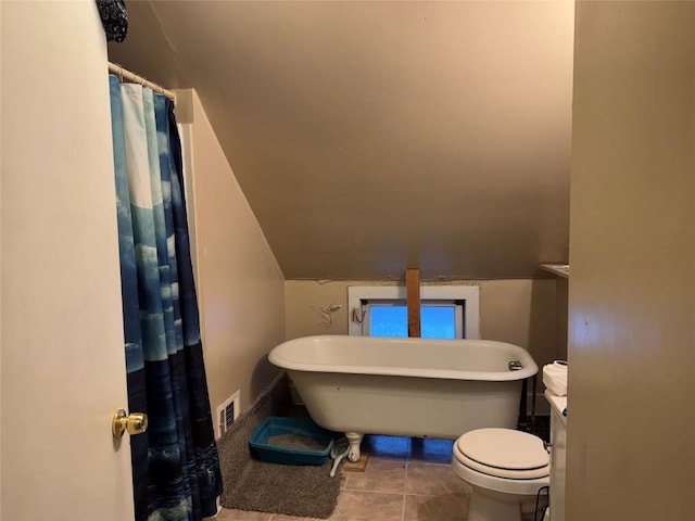 bathroom featuring toilet, vaulted ceiling, tile patterned floors, and a tub to relax in