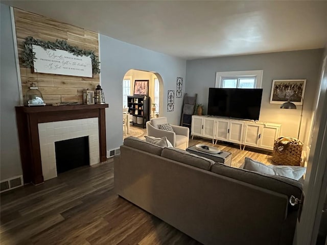 living room featuring a tiled fireplace and dark wood-type flooring