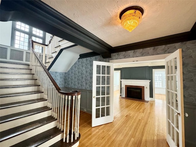 staircase featuring french doors, a brick fireplace, a textured ceiling, wood-type flooring, and beamed ceiling