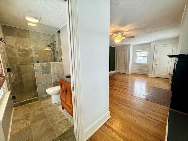 bathroom featuring vanity, a shower with door, hardwood / wood-style flooring, ceiling fan, and toilet