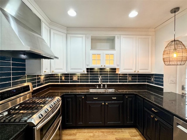 kitchen with wall chimney range hood, sink, dark stone countertops, white cabinetry, and stainless steel appliances