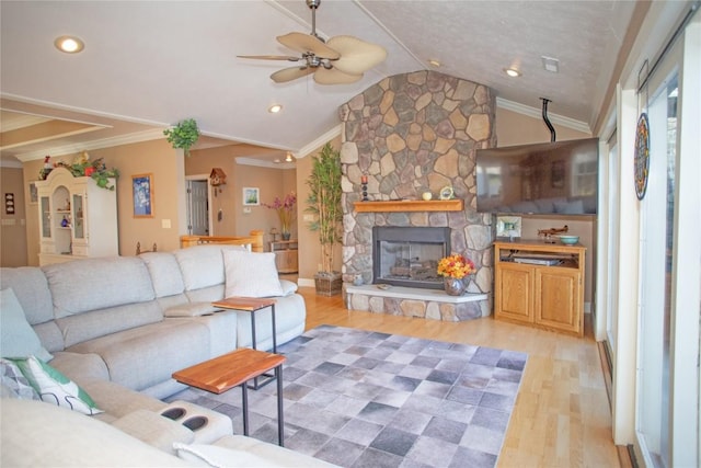 living room with ceiling fan, a stone fireplace, light hardwood / wood-style flooring, vaulted ceiling, and ornamental molding