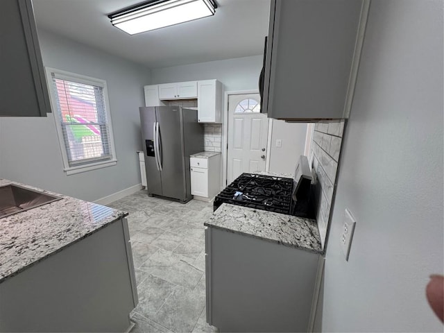 kitchen featuring stove, tasteful backsplash, light stone counters, and stainless steel refrigerator with ice dispenser