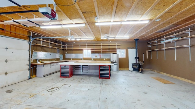 garage featuring a workshop area, a garage door opener, stainless steel refrigerator, and a wood stove