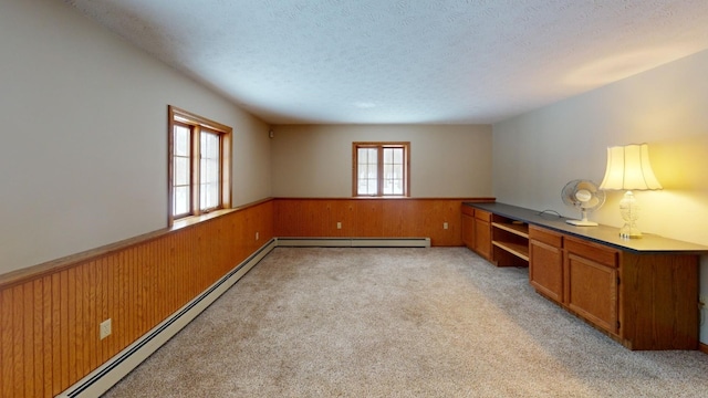 unfurnished office with a textured ceiling, baseboard heating, wooden walls, and light carpet