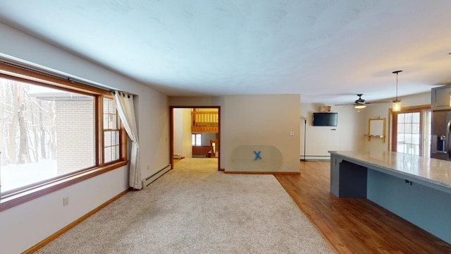 unfurnished living room with ceiling fan, a healthy amount of sunlight, and a baseboard heating unit