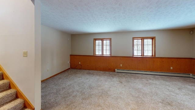 unfurnished room with a baseboard heating unit, a textured ceiling, light colored carpet, and wooden walls