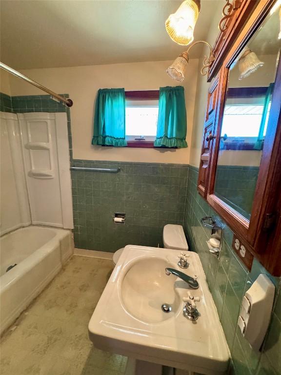 bathroom with a wainscoted wall, toilet, bathing tub / shower combination, tile walls, and a sink