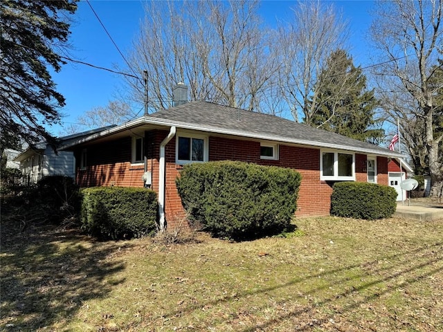 view of side of property featuring brick siding, a lawn, a chimney, and roof with shingles