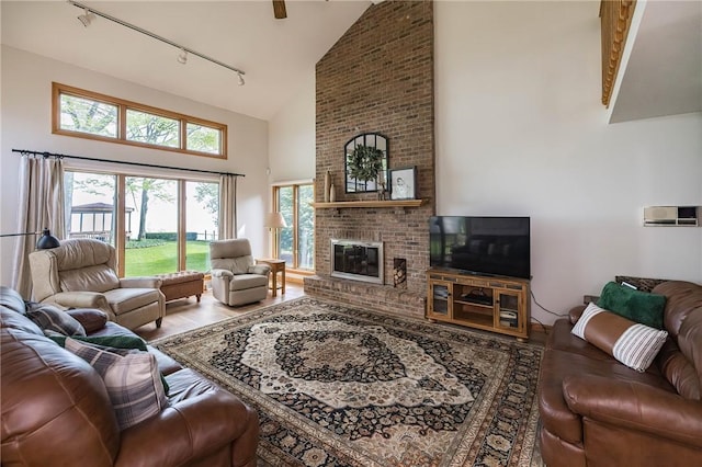 living room with hardwood / wood-style floors, track lighting, high vaulted ceiling, and a brick fireplace