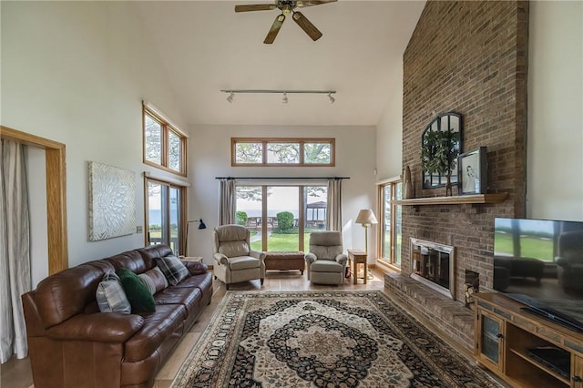 living room with ceiling fan, rail lighting, a towering ceiling, wood-type flooring, and a fireplace