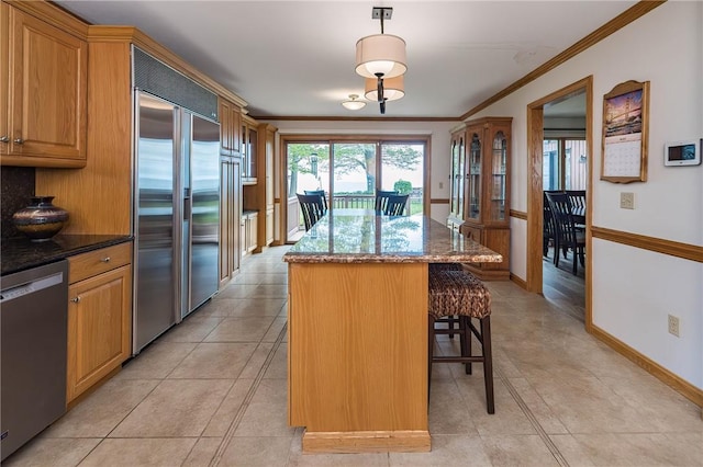 kitchen featuring hanging light fixtures, crown molding, dark stone counters, a kitchen island, and appliances with stainless steel finishes