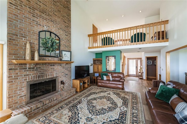 living room featuring a brick fireplace, a towering ceiling, and hardwood / wood-style flooring