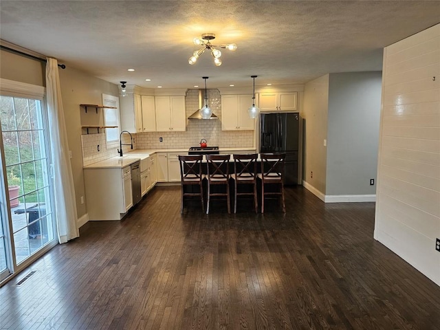 kitchen featuring black refrigerator with ice dispenser, sink, stainless steel dishwasher, decorative light fixtures, and a kitchen island