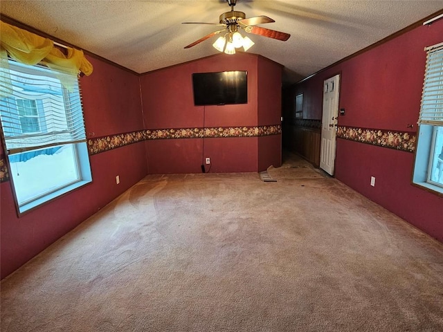 empty room featuring a textured ceiling, vaulted ceiling, ceiling fan, crown molding, and carpet floors