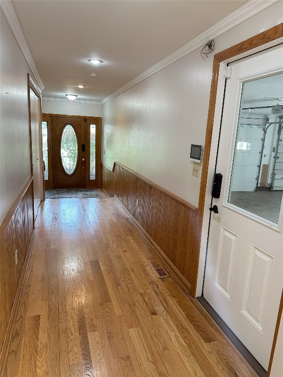 doorway with light hardwood / wood-style flooring, crown molding, and wood walls