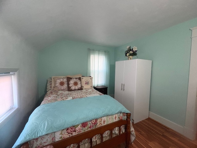 bedroom with vaulted ceiling, wood finished floors, and baseboards