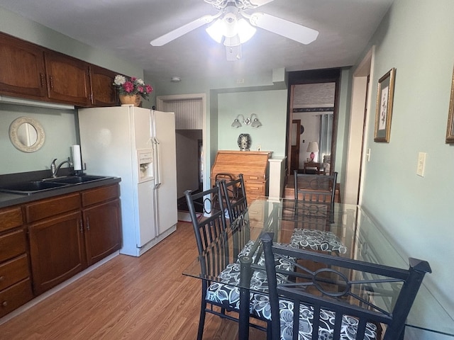 kitchen with light wood finished floors, a sink, a ceiling fan, white fridge with ice dispenser, and dark countertops