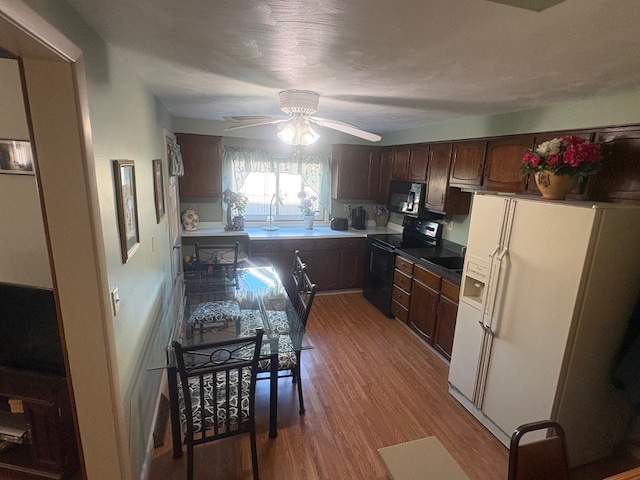 kitchen with wood finished floors, dark brown cabinets, black appliances, ceiling fan, and a sink
