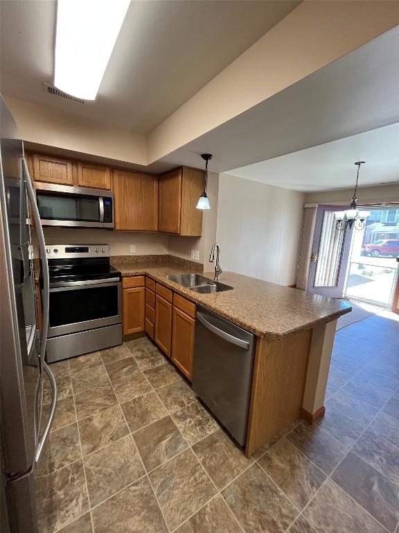 234 Walnut St Unit 13, Meadville, PA 16335 - kitchen with stainless steel appliances, a sink, a peninsula, brown cabinetry, and hanging light fixtures