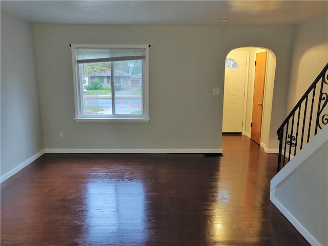 empty room featuring arched walkways, stairway, baseboards, and wood finished floors