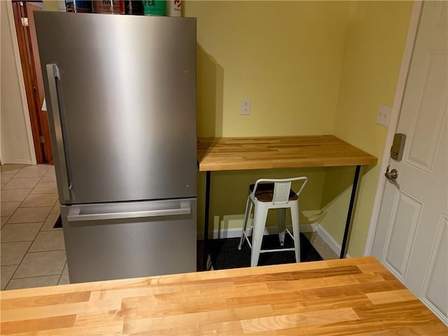 kitchen with butcher block countertops, freestanding refrigerator, tile patterned flooring, and baseboards