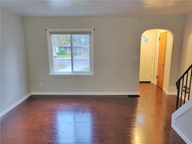 unfurnished room featuring dark wood-style floors, arched walkways, baseboards, and stairs