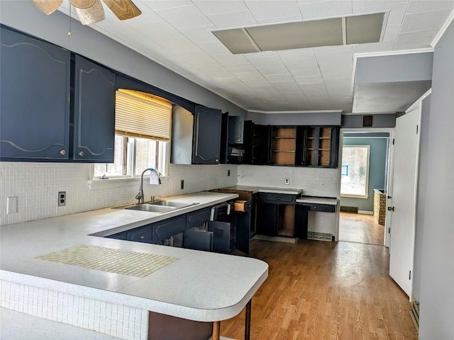 kitchen with kitchen peninsula, decorative backsplash, ceiling fan, sink, and light hardwood / wood-style floors