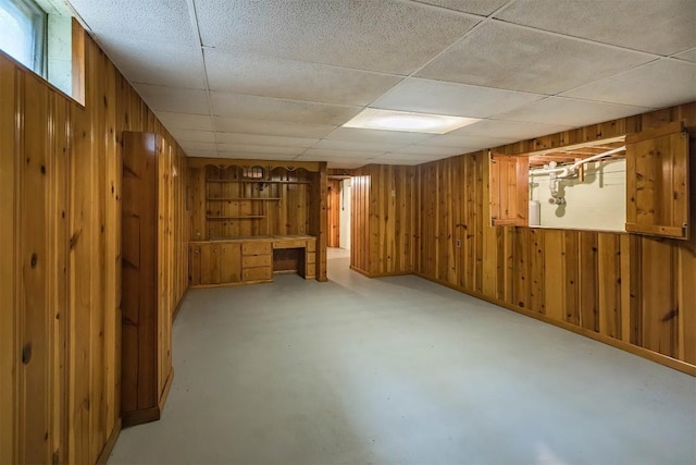 basement featuring a paneled ceiling, wood walls, and built in desk